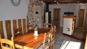 A dining area with a wooden table and chairs, a clock on the wall, and a stone wall. - CHARMING HOUSE ON THE EDGE OF CEVENNES NATIONAL PARK (Meyrueis)