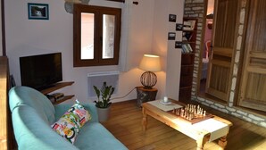 A cozy living room with a sofa, a TV, a lamp, and a chess table. - CHARMING HOUSE ON THE EDGE OF CEVENNES NATIONAL PARK (Meyrueis)