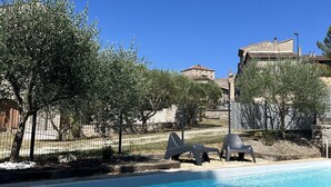 En swimmingpool med kristallklart blått vatten, omgiven av olivträd och ett staket.