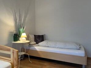 Een minimalistische slaapkamer met een bed, nachtkastje, lamp en decoratieve planten.