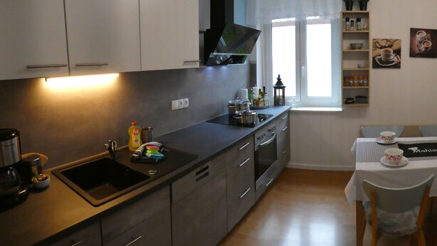 A modern kitchen with a sink, stove, and cabinets. There is a window with curtains and a table with chairs in the dining area. - Allgäutraum Apartment No. 1 for 2-4 people in Durach-Weidach (Oberkottern)
