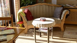 A cozy room with a wooden bench, a small round table with a lace tablecloth, and a striped sofa with a red blanket and a pillow.