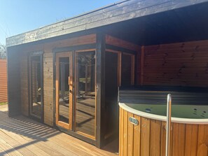 Un patio in legno con vasca idromassaggio e una zona coperta con vetrate.