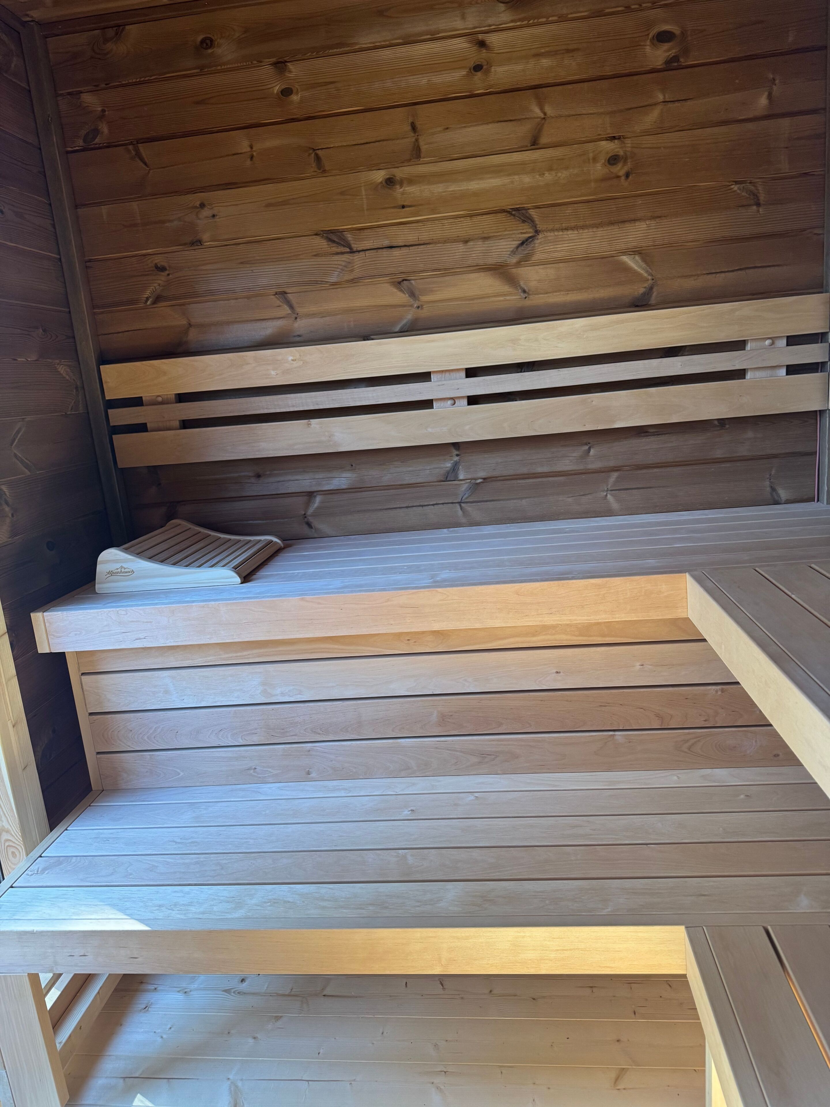 Un banc en bois doté d’un dossier à lattes et d’une assise plate, placé contre un mur recouvert de planches de bois disposées horizontalement.