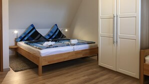 Quarto com cama de madeira, duas almofadas, mesa de cabeceira e guarda-roupa.
