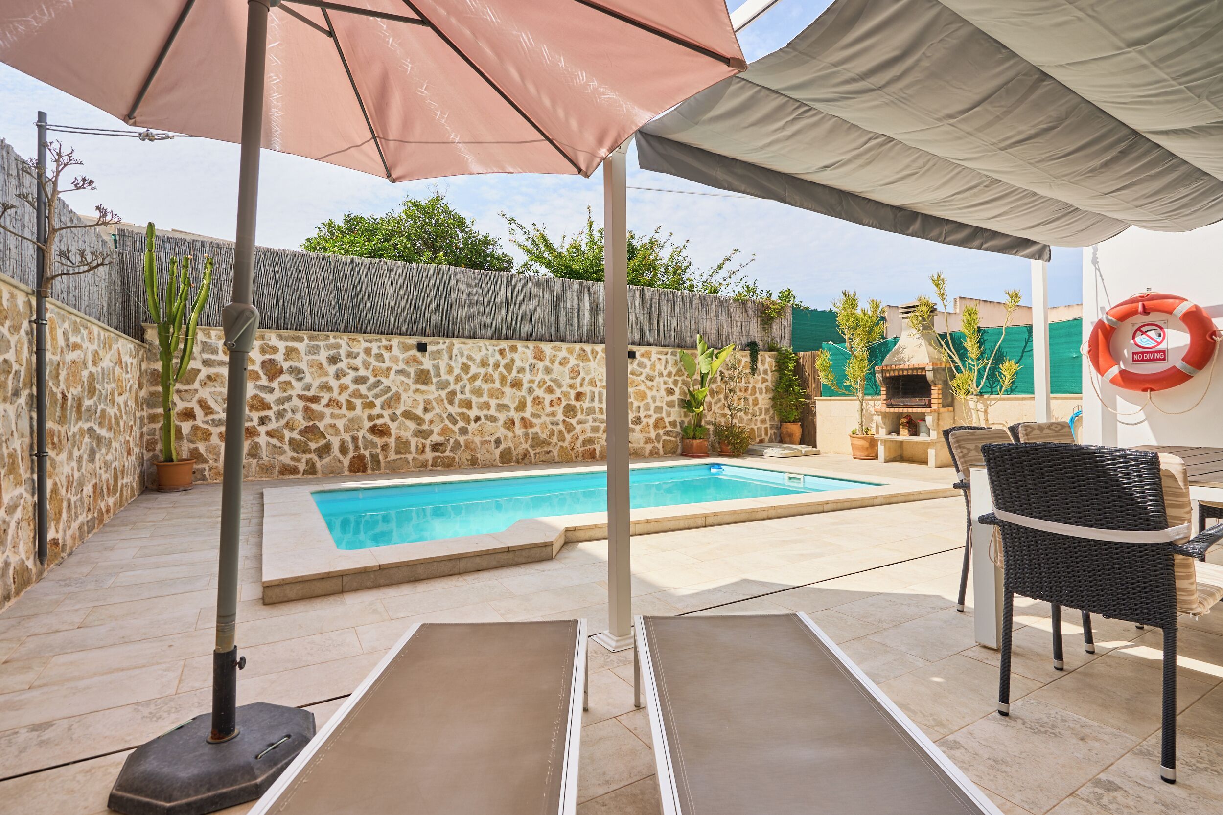 A backyard with a swimming pool, lounge chairs, a barbecue area, and a stone wall.