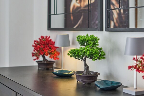 Une table en bois foncé, sur laquelle sont disposés trois petits arbres bonsaï en pot : deux avec des feuilles rouges et un avec des feuilles vertes, ainsi que deux bols décoratifs.