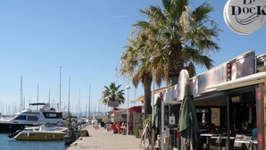 Un port de plaisance avec des bateaux amarrés, une promenade pavée et un restaurant appelé « Le Dock », doté d’une terrasse.