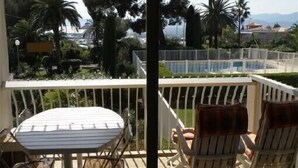 Un balcon avec une table et deux chaises, donnant sur une piscine et un espace verdoyant.