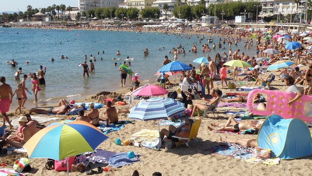 Une plage bondée où les gens se prélassent au soleil et se baignent.