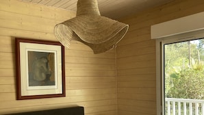 Ein Schlafzimmer mit einem Bett, einem gerahmten Kunstwerk, einer Pendelleuchte, einem Nachttisch mit Radio und Blick auf einen Balkon mit einem Stuhl.