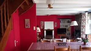 Un comedor con mantel a cuadros, sillas de madera, chimenea, estantería y escalera.