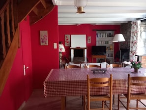 Un'area pranzo con tovaglia a scacchi, sedie in legno, un camino, una libreria e una scala.