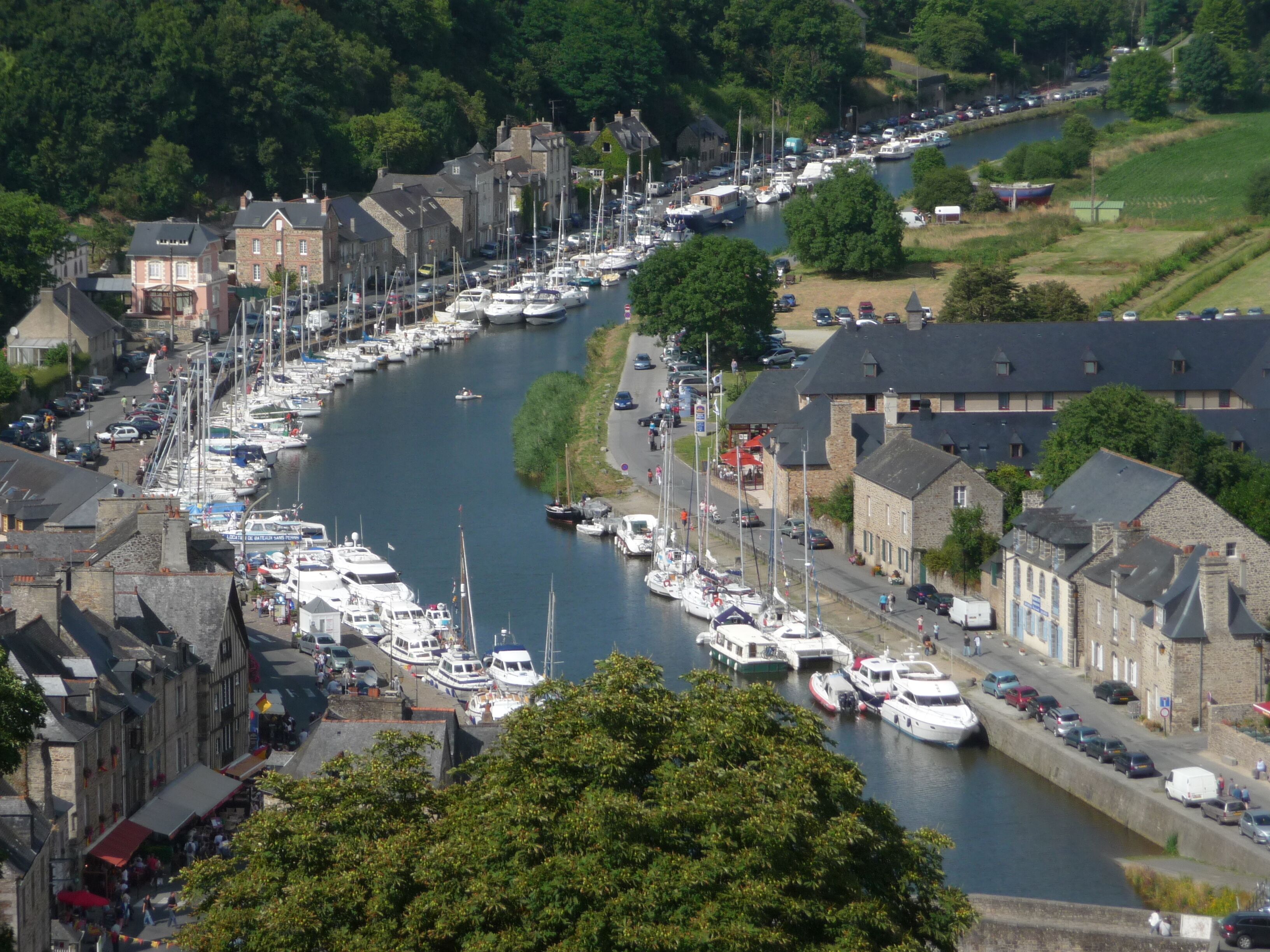 A riverside town with a marina filled with boats, historic stone buildings, and a narrow road alongside the water.