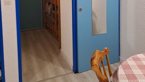 Huone, jossa on sininen ovi, puinen tuoli ja sängyssä ruutukuosinen peitto.