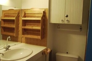 Un baño con lavamanos, estantes de madera y un inodoro.