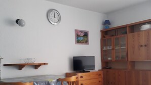 Ruokailutila, jossa on pöytä, tuoleja, televisio, kello ja puiset kaapit.