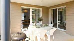 Un patio al aire libre con una mesa lista para comer, rodeado de sillas blancas.