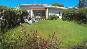 Una casa con un césped cuidado, un patio con dos sillones de descanso y un pequeño jardín con diversas plantas y flores.