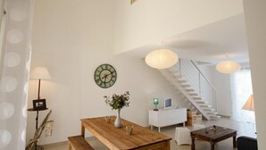 Un salón amplio con una mesa de comedor de madera, un sofá blanco, una escalera y un reloj en la pared.