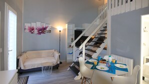 A compact living space with a sofa, dining table, and staircase. - Apartment SOULAC SUR MER 500 m from the beach 3 (Soulac-Sur-Mer)