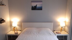 A bedroom with a large bed, two bedside tables with lamps, a wall-mounted picture, and a sloped ceiling. - Apartment SOULAC SUR MER 500 m from the beach 3 (Soulac-Sur-Mer)