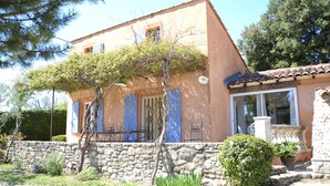 Edificio de dos plantas con un muro de piedra, un árbol en frente y un pequeño jardín.