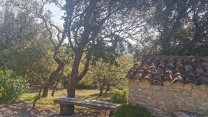 Un muro de piedra con tejado de baldosas, un banco de madera y árboles en un jardín.