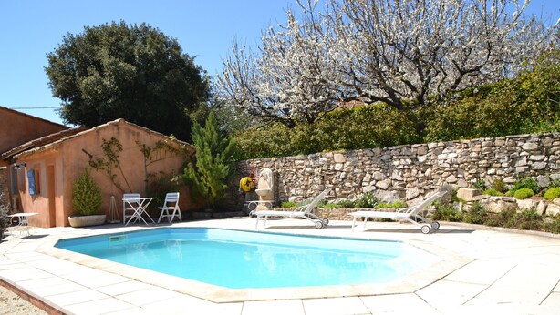 Una piscina rectangular con un muro de piedra y un edificio pequeño al fondo.