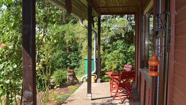 Een overdekt terras met houten vloer, een tafel en stoelen, en een lantaarn.