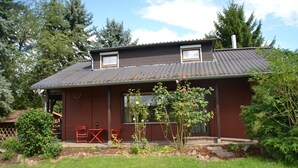 Een huis met twee verdiepingen, een bruine gevel, een metalen dak en een klein portaal met rode stoelen.