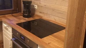 Een keuken met een zwarte inductiekookplaat, een ingebouwde oven, een koffiezetapparaat en een houten aanrecht.