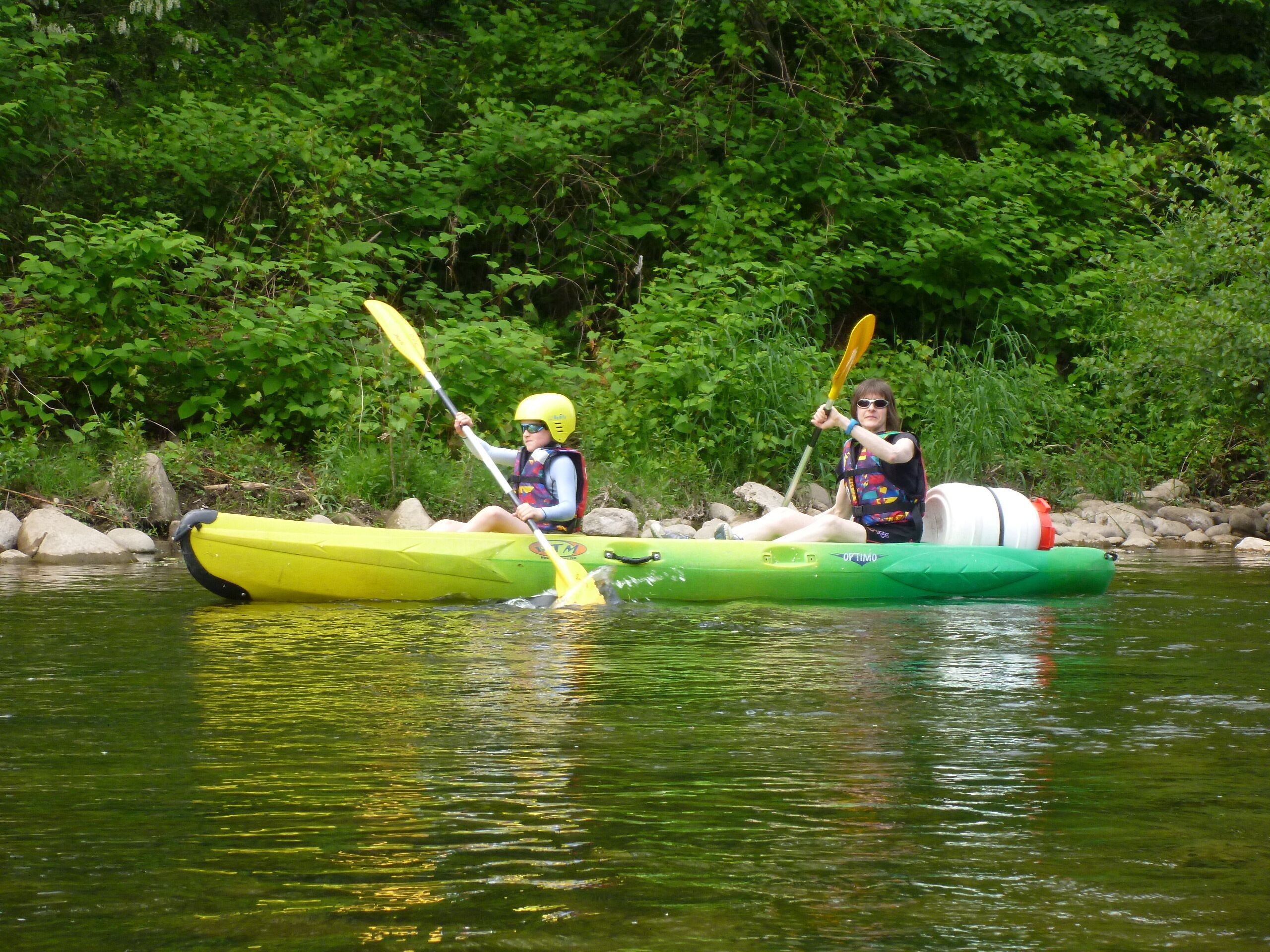 Deux personnes pratiquent le kayak sur une rivière bordée de verdure.