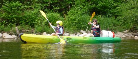 Deux personnes pratiquent le kayak sur une rivière bordée de verdure.