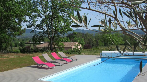 A swimming pool with lounge chairs, surrounded by trees and a view of the countryside.