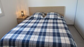 A bedroom with a checkered bedspread, two pillows, a nightstand with a lamp, and a window.