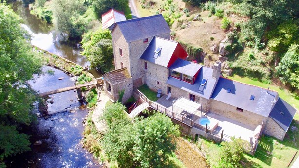 Un bâtiment en pierre doté d’une extension moderne, une piscine et une rivière à proximité.