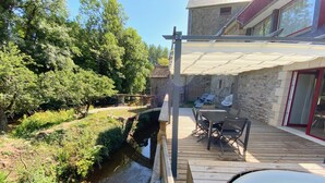 Une terrasse en bois avec une table et des chaises, un jacuzzi et un bâtiment en pierre avec un toit rouge.