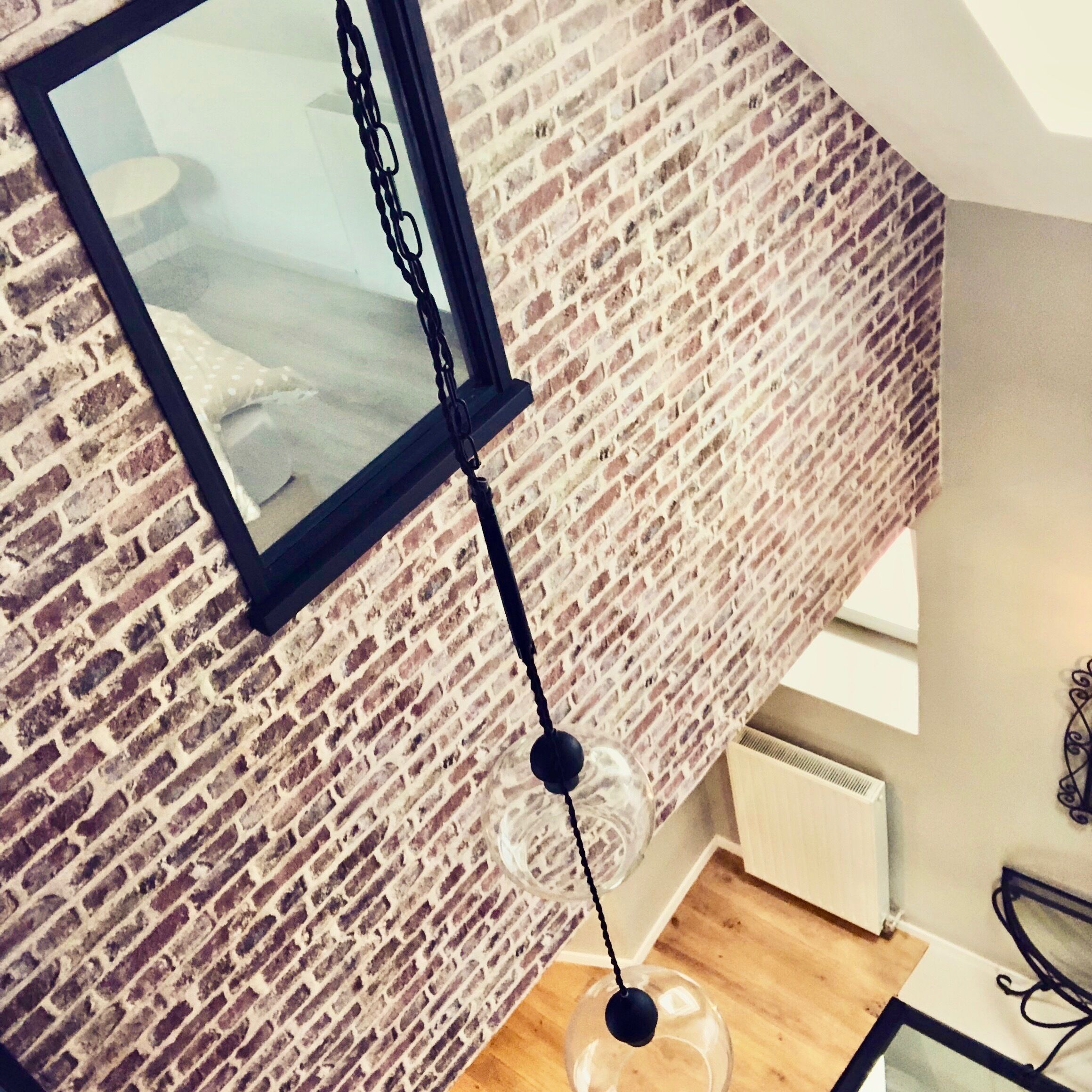 A room with a brick wall, a hanging light fixture, and a framed picture.
