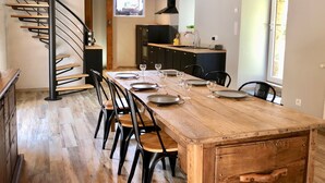 Une cuisine moderne avec une table à manger en bois pour quatre personnes, un escalier en colimaçon et une vue sur l’extérieur.