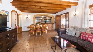 A spacious living area with a high wooden ceiling, a dining set, a sofa, and a television.