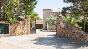 A stone-walled entrance with a metal gate, a stone building with a tiled roof, and a clear sky.