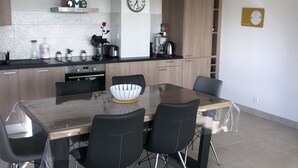 Eine moderne Küche mit Essbereich. Sie umfasst einen Herd, ein Waschbecken und Schränke. An der Wand hängt eine Uhr und auf dem Tisch steht eine Schüssel.