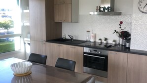 Eine moderne Küche mit Holdekor-Schränken, einer schwarzen Arbeitsplatte und Edelstahlgeräten. Ein Esstisch mit Stühlen und eine Vase mit einer Rose stehen auf der Arbeitsplatte.