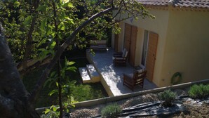 Eine Terrasse mit Gartenmöbeln, ein kleiner Garten und ein Gebäude mit Ziegeldach.
