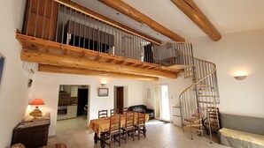 Ein geräumiger Wohnbereich mit hohen Decken und freiliegenden Holzbalken, ein Essbereich mit Tisch und Stühlen sowie eine Wendeltreppe zu einer oberen Ebene.