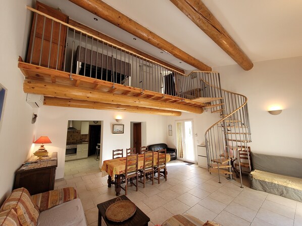 A spacious living area with a high ceiling and exposed wooden beams, a dining area with a table and chairs, and a spiral staircase leading to an upper level.