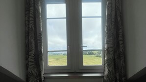 A room with a window overlooking a landscape, a wooden table with a plaque, and patterned curtains. - !!!Studio less than 50 meters from the sea !!!28 € / Night and 35 € / summer for 2 people (Veulettes-sur-Mer)