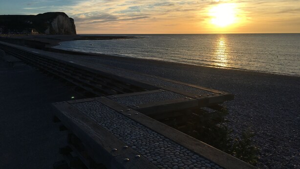 A beach with a wooden walkway leading to the water, a cliff in the background, and the sun setting over the horizon. - !!!Studio less than 50 meters from the sea !!!28 € / Night and 35 € / summer for 2 people (Veulettes-sur-Mer)