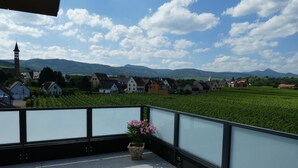 En balkon med udsigt over en landsby, et kirketårn og grønne marker.